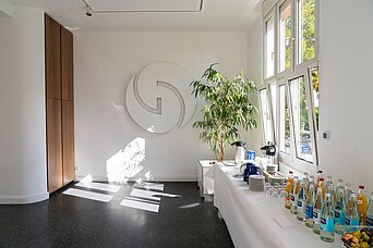Lichtdurchfluteter Raum, weiße Wände, rechts Getränke auf Tisch mit weißer Tischdecke
